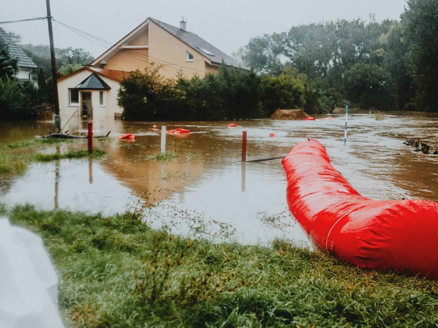 Residential flood mitigation with red water barrier protecting a flooded home.