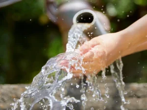 Clean water flowing over child’s hands from outdoor pipe illustrating water mitigation and protection in Florida