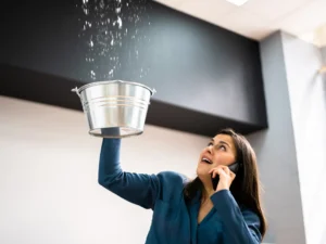 What to do after a water leak in Florida, woman catching ceiling leak with bucket while on phone